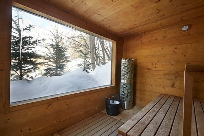 Wood sauna with large picture window and snowy forest views