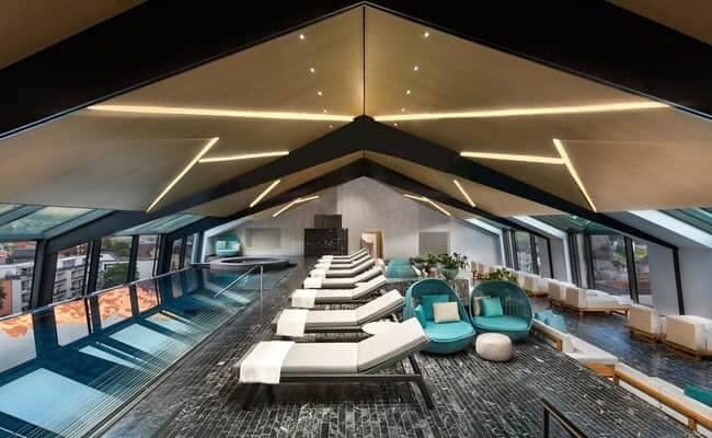 Glass-walled indoor pool with loungers and panoramic city views