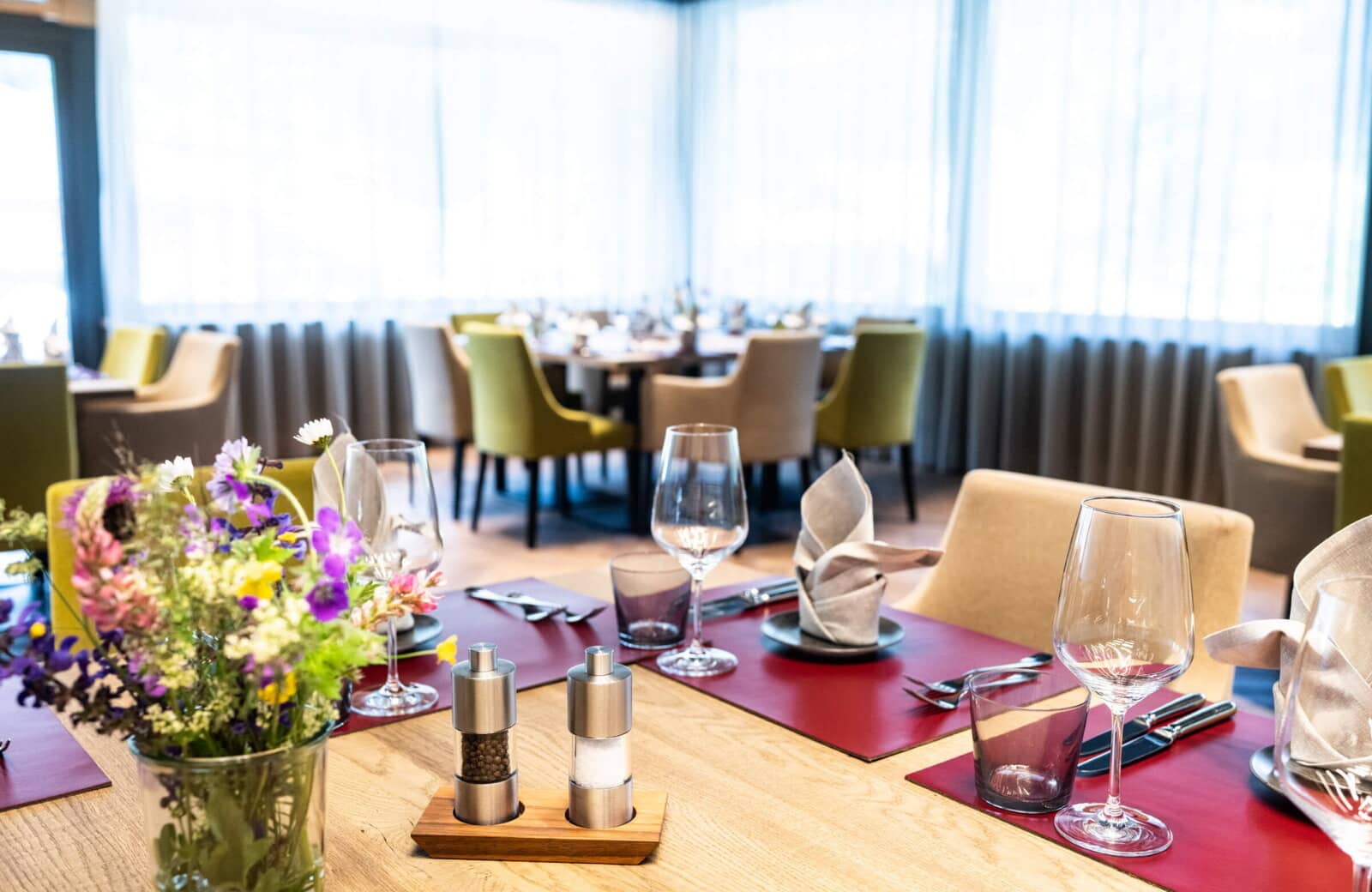 Dining area with tables set for 8; floor-to-ceiling windows with privacy curtains