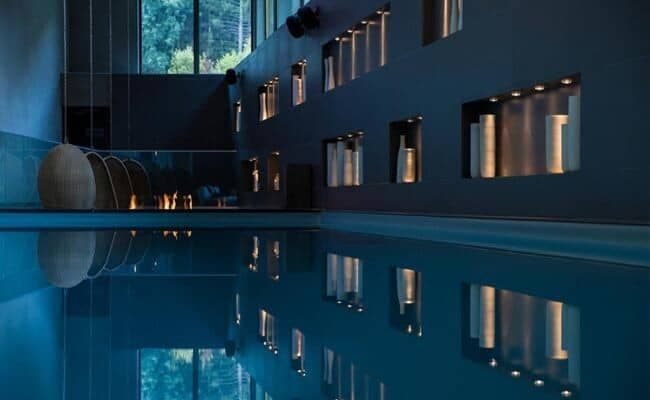 Indoor heated pool with fireplace and illuminated wall alcoves