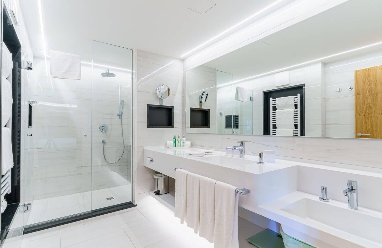 Bathroom with dual vanity, walk-in rainfall shower, and heated towel rack