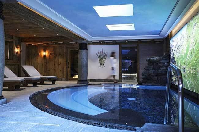 Indoor pool with waterfall feature, lounge seating, and adjacent sauna access
