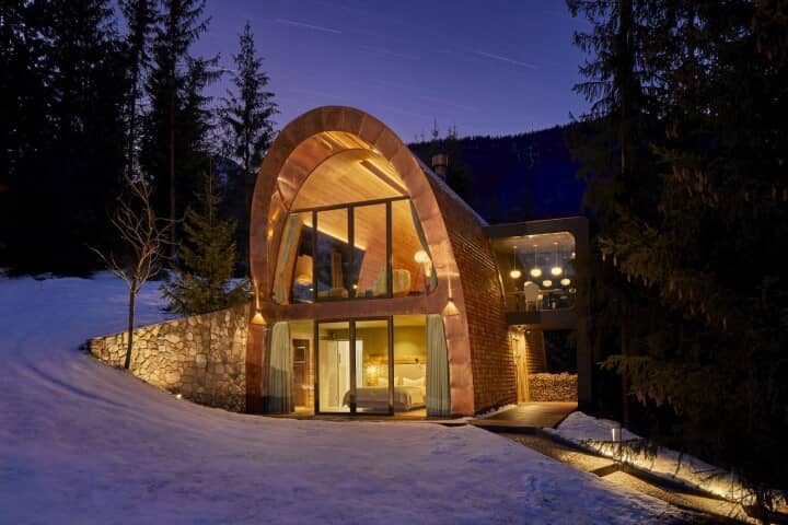 Two-story mountain cabin with floor-to-ceiling windows and covered wood storage