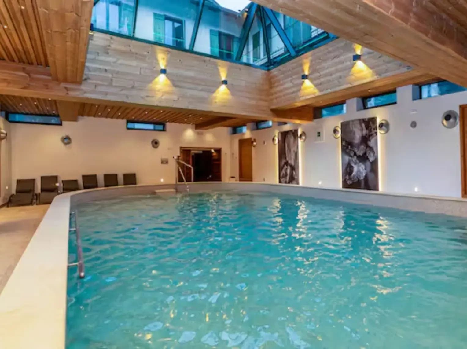 Indoor pool with glass atrium ceiling and poolside lounge seating