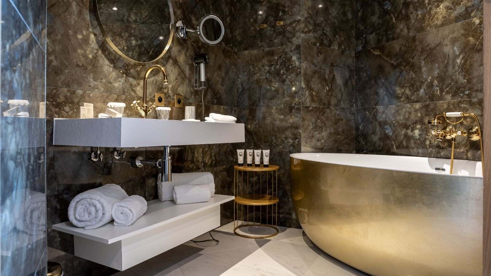 Bathroom with gold soaking tub and dark stone tile walls