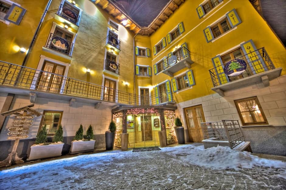 Courtyard entrance with yellow restored facades, heated ground-level lighting, and hotel reception