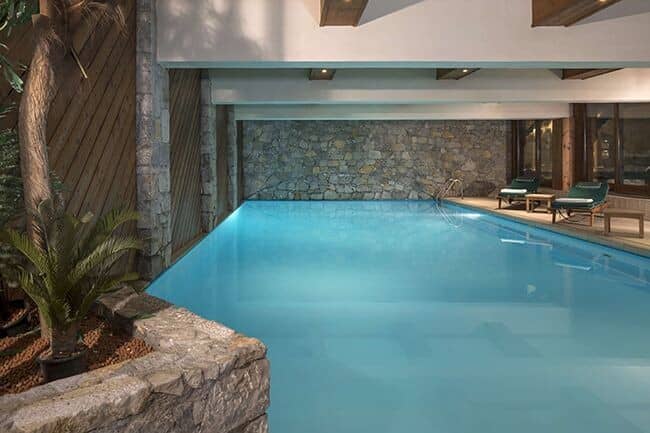 Indoor heated pool with stone feature wall and poolside lounge chairs