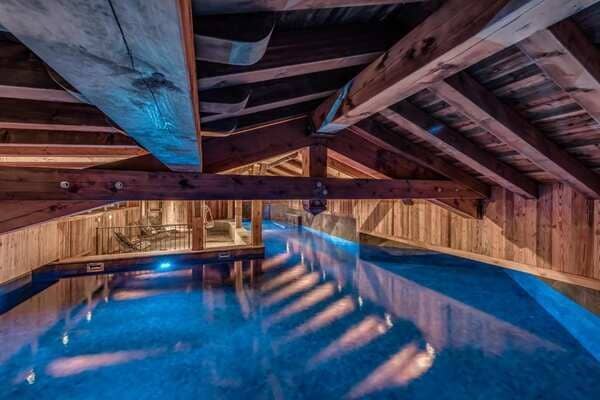 Indoor heated pool with exposed timber beams and poolside lounge seating