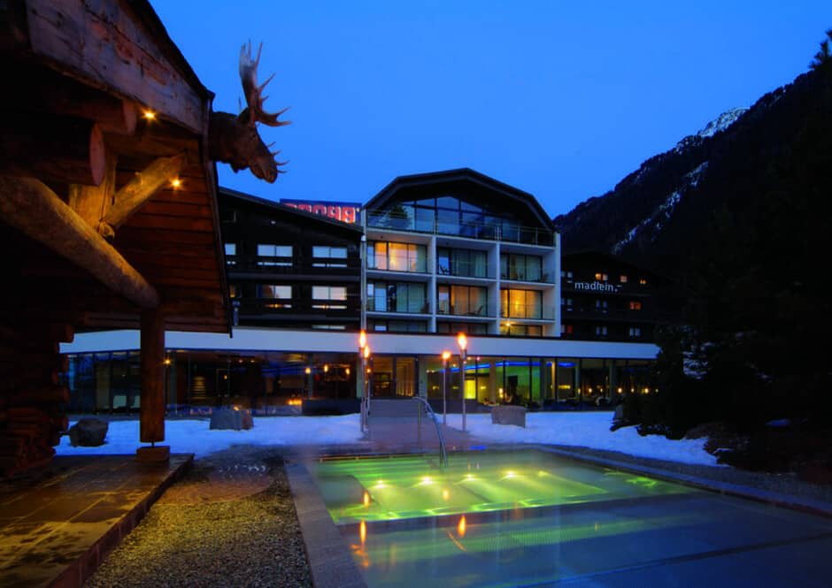 Heated outdoor pool with mountain backdrop and illuminated lodge facade