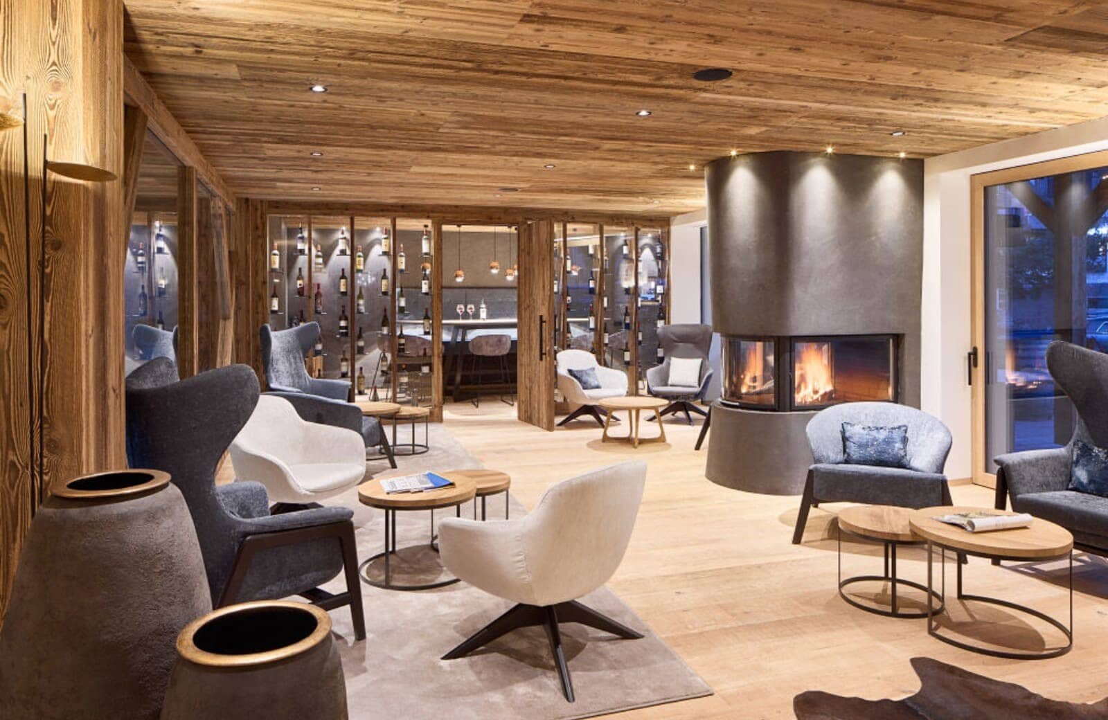 Lounge with wood-paneled ceiling, circular fireplace, and glass-enclosed wine cellar