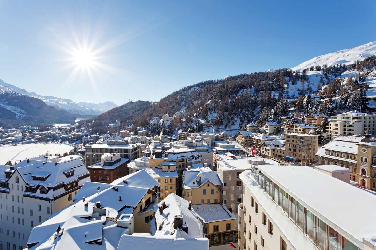 City and mountain views from balcony; overlooking snow-covered village rooftops