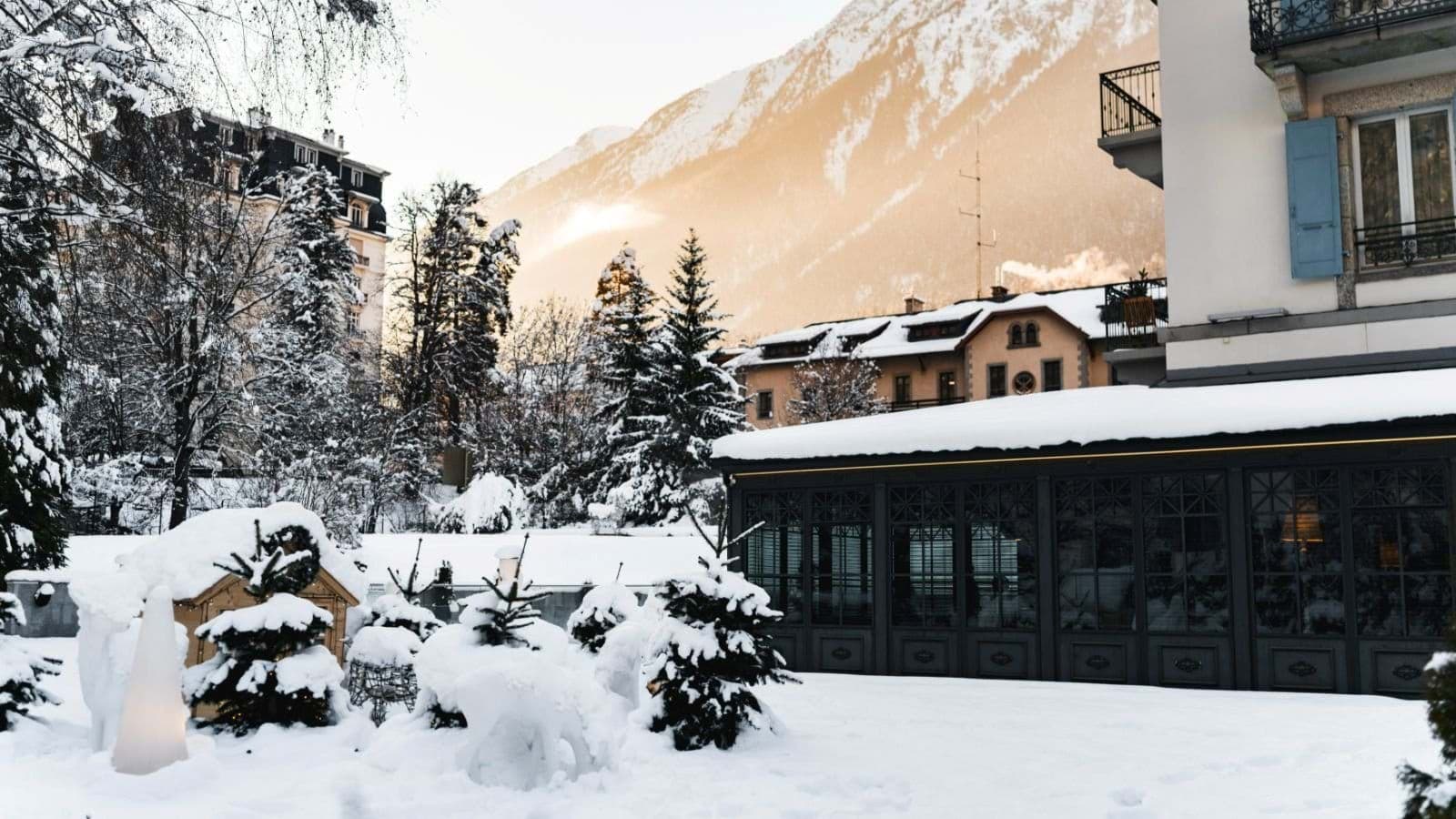 Snow-covered garden courtyard with alpine mountain views and glass-enclosed sunroom