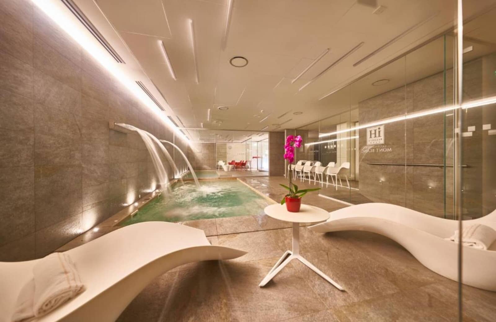 Indoor spa pool featuring wall-mounted waterfalls and ergonomic lounge seating
