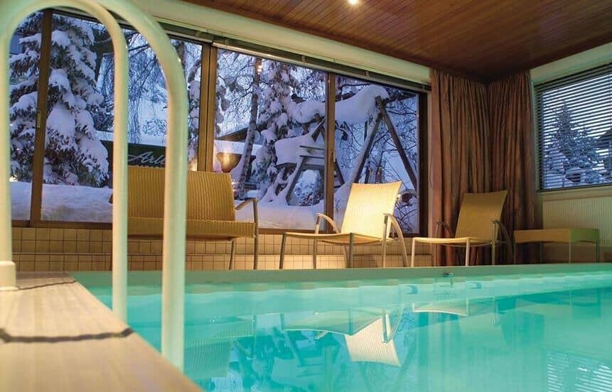 Indoor heated pool with poolside lounge seating and snowy garden views