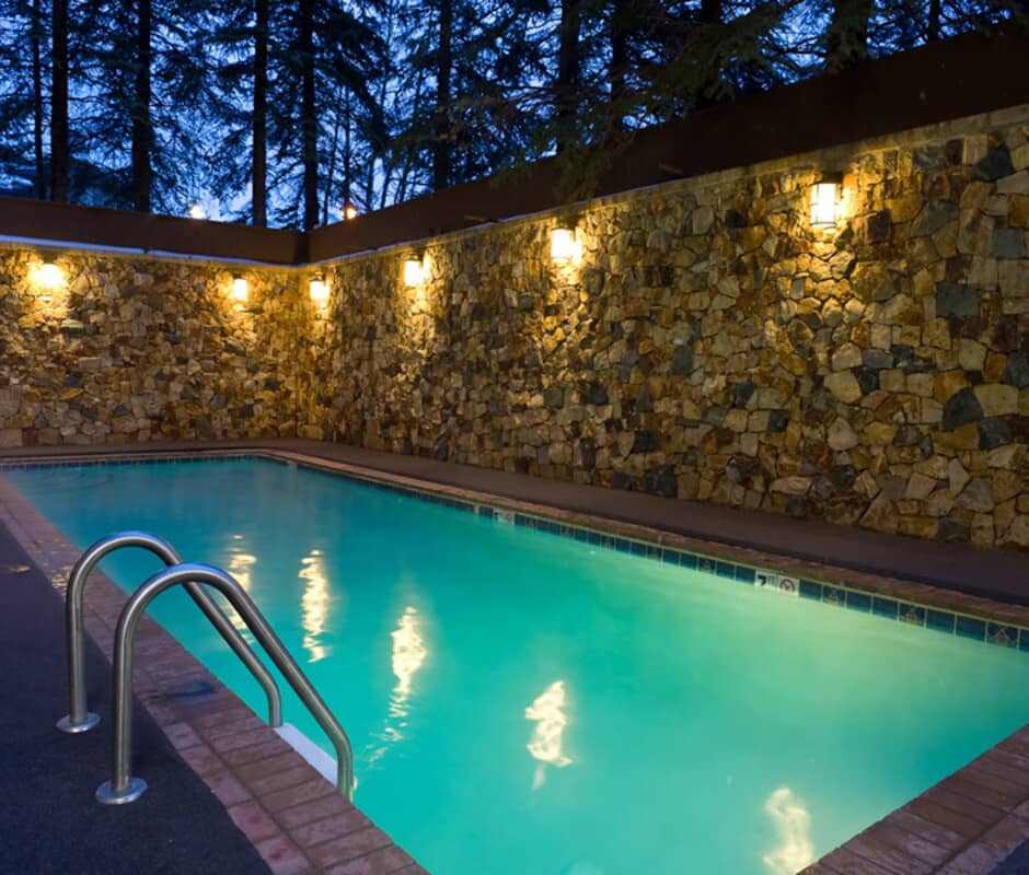 Outdoor pool with stone privacy wall and evening lighting