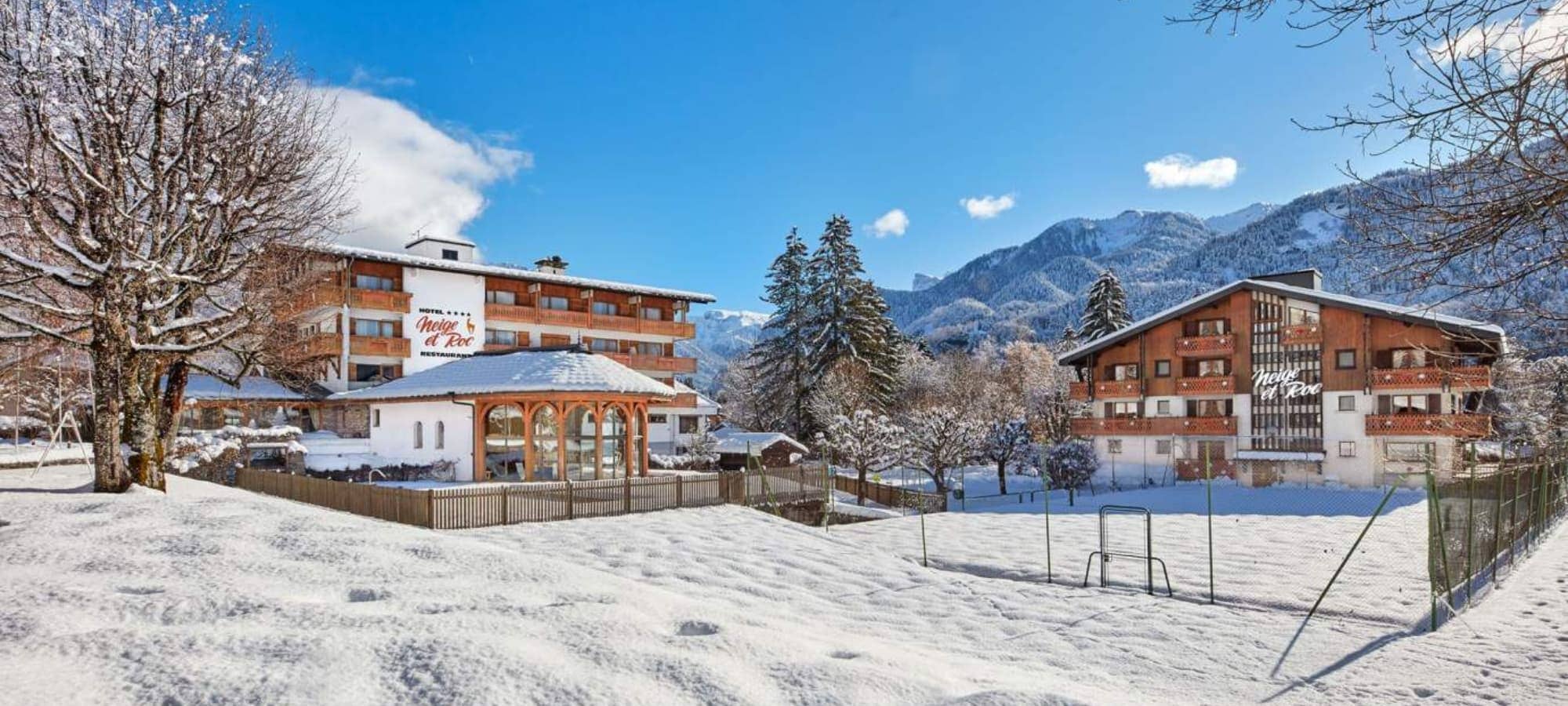 Hotel exterior with snow-covered tennis court and mountain views