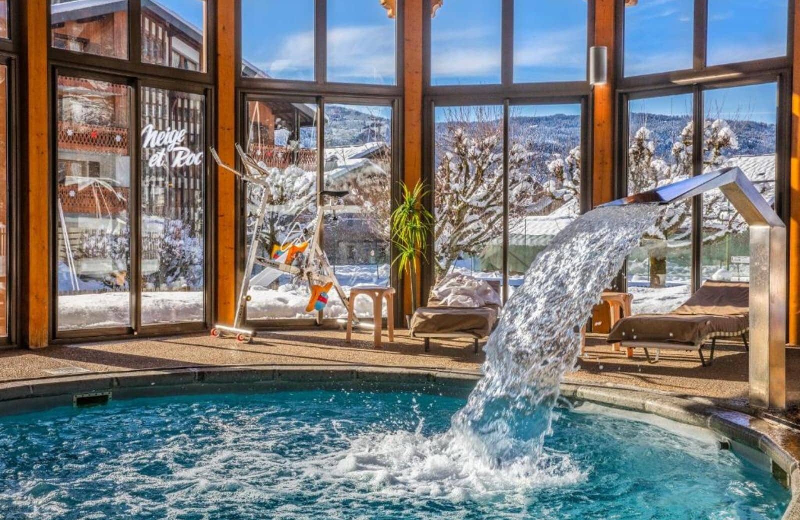 Indoor pool with waterfall feature and floor-to-ceiling mountain views
