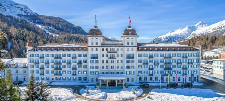 Hotel exterior featuring blue shutters and snow-covered mountain backdrop