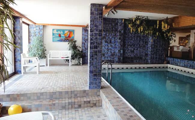 Indoor heated pool area with tile deck and poolside seating