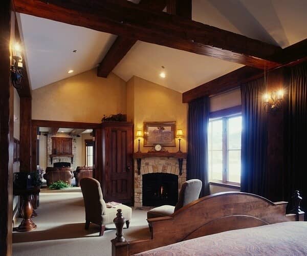 Primary bedroom with stone fireplace, vaulted wood beams, and sitting area