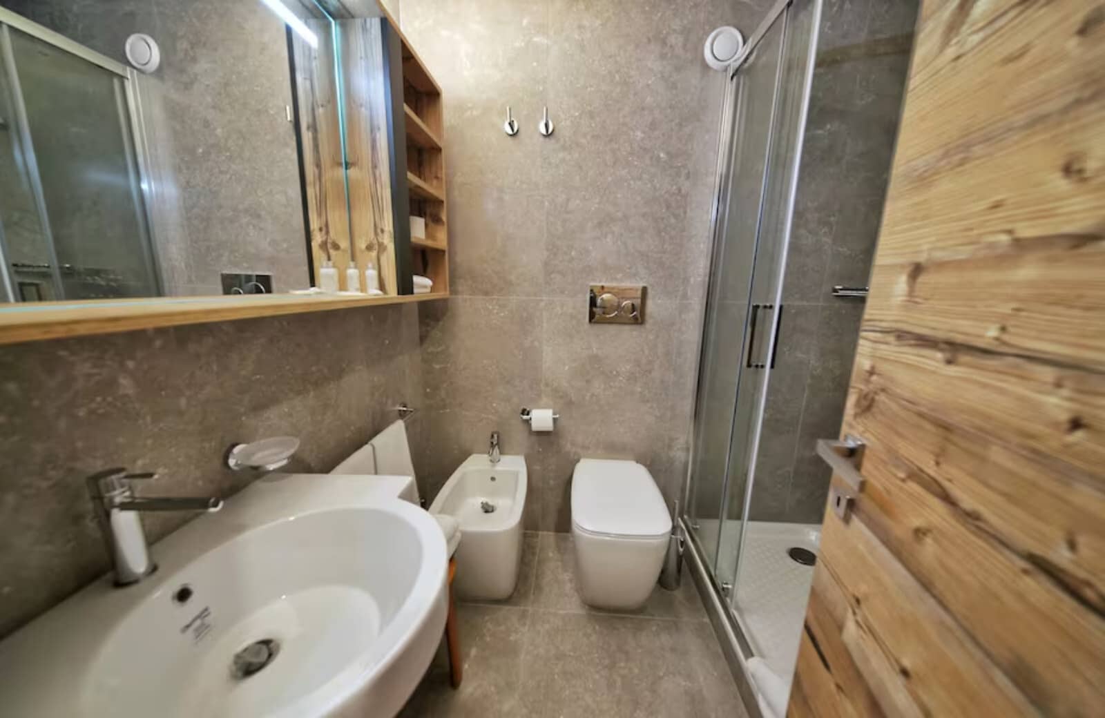 Bathroom with glass walk-in shower, bidet, and stone-tiled walls