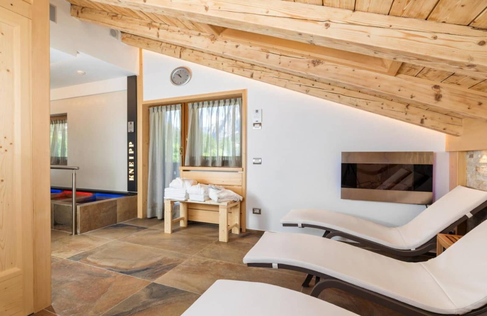 Spa relaxation room with loungers, wall fireplace, and Kneipp hydrotherapy pool