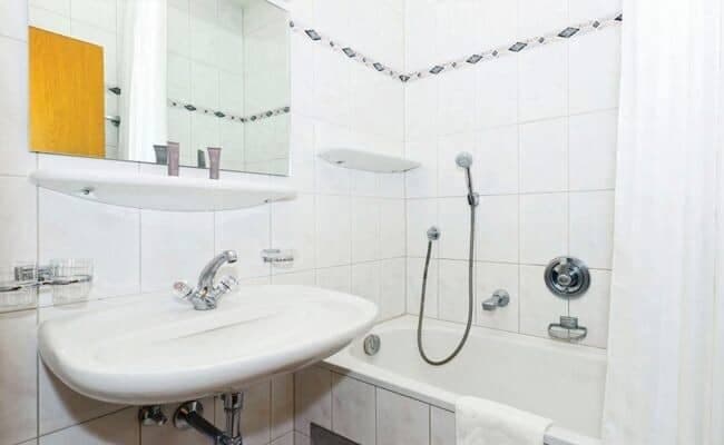 Bathroom featuring pedestal sink and tiled bathtub with handheld shower attachment