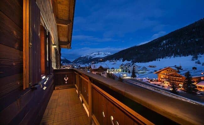 Private wooden balcony overlooking snow-covered alpine village and mountain peaks