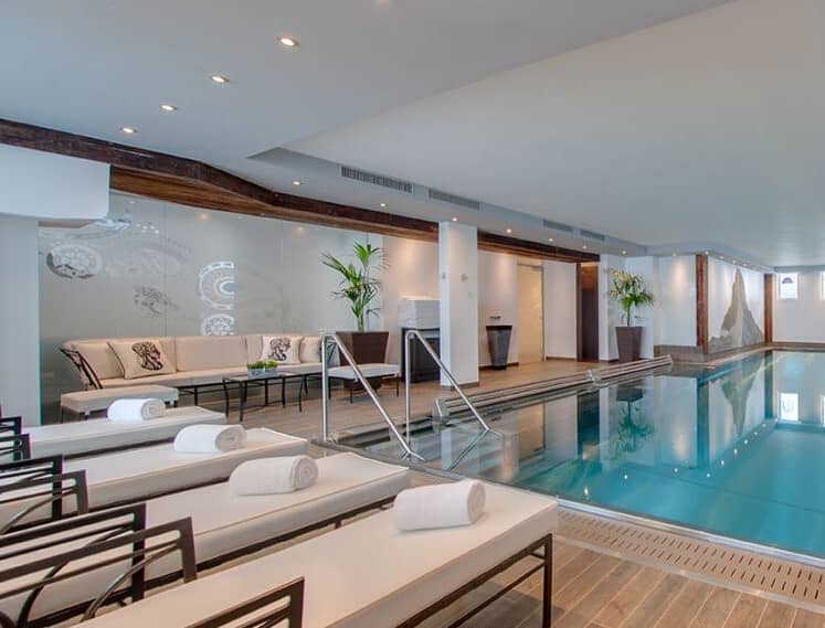 Indoor heated lap pool with poolside loungers and sofa seating