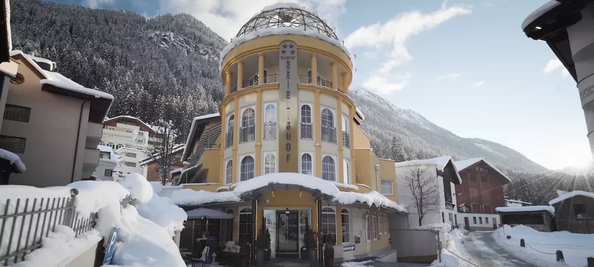 Hotel exterior with glass-domed tower and mountain forest backdrop
