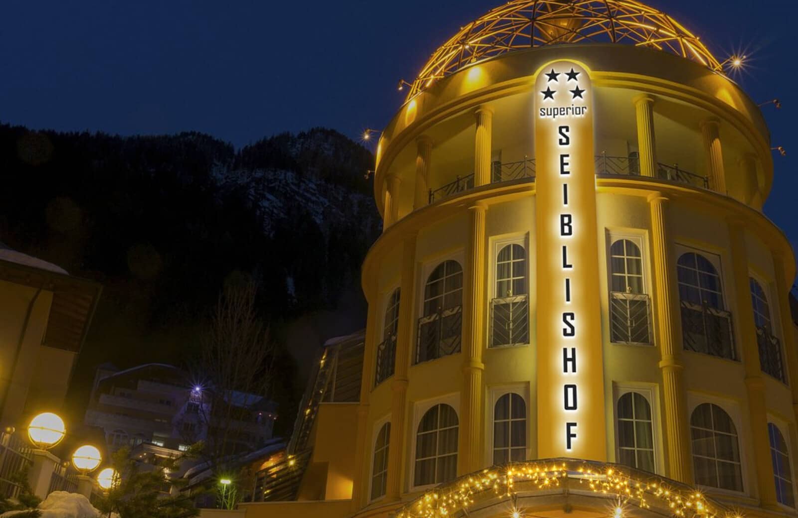 Hotel exterior at night with illuminated facade and mountain backdrop