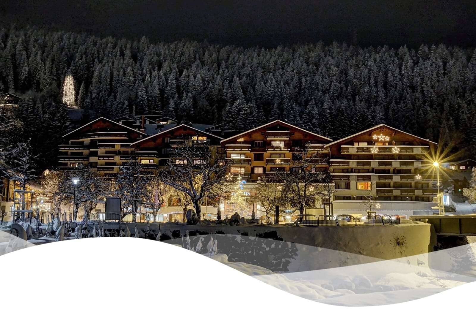 Resort exterior at night with private balconies and wooded mountain backdrop