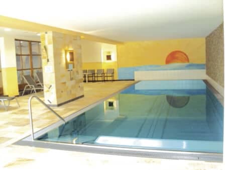 Indoor swimming pool with handrail access and poolside lounge chairs