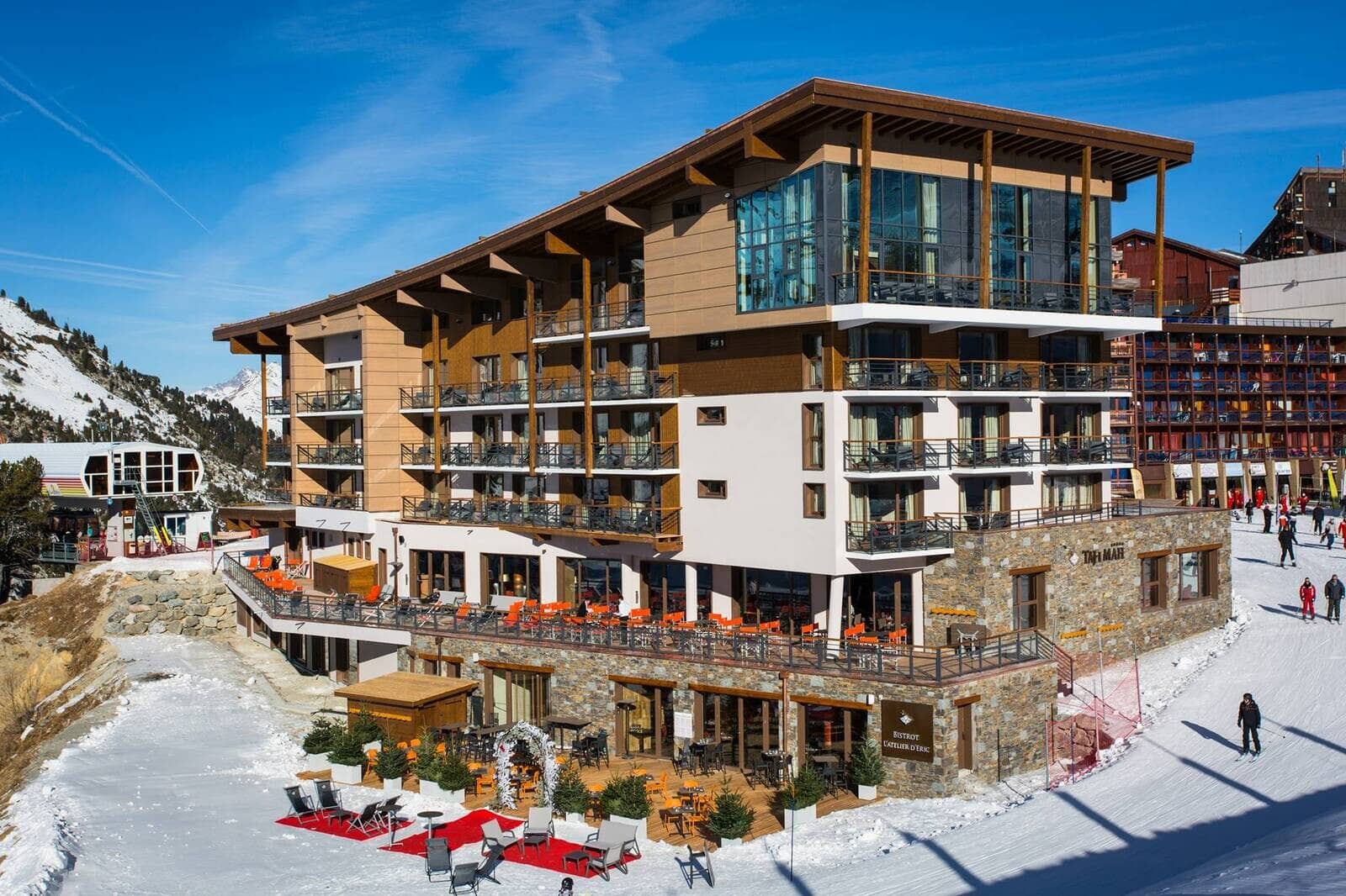 Alpine resort building with wood-beam architecture and ground-floor dining terrace overlooking slopes