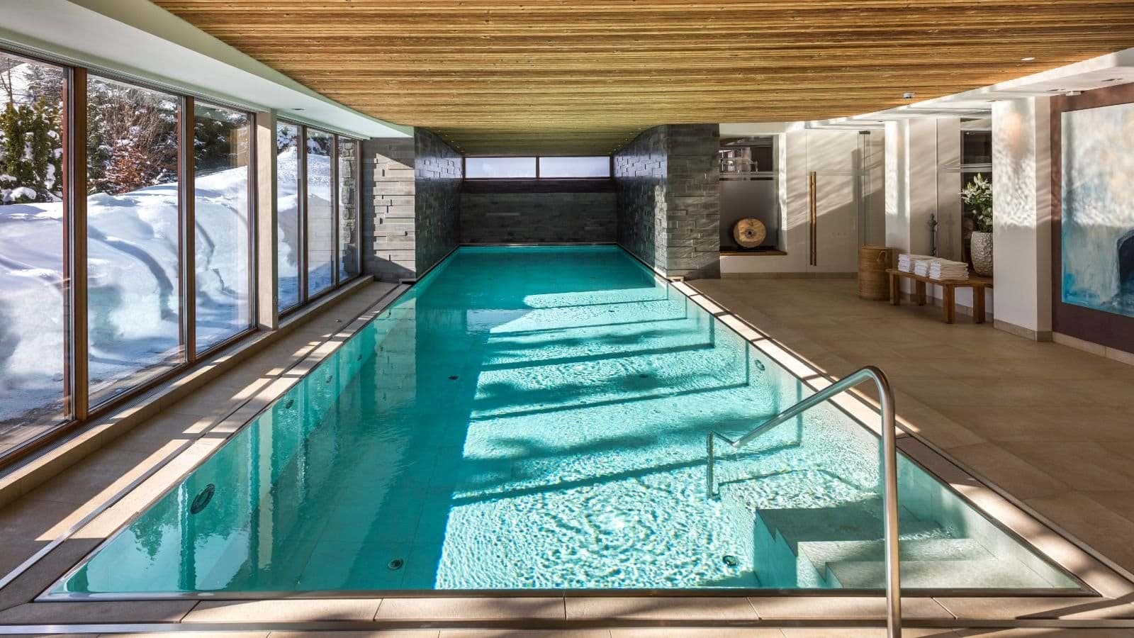 Indoor lap pool with wood-slat ceiling and snow-covered terrace views
