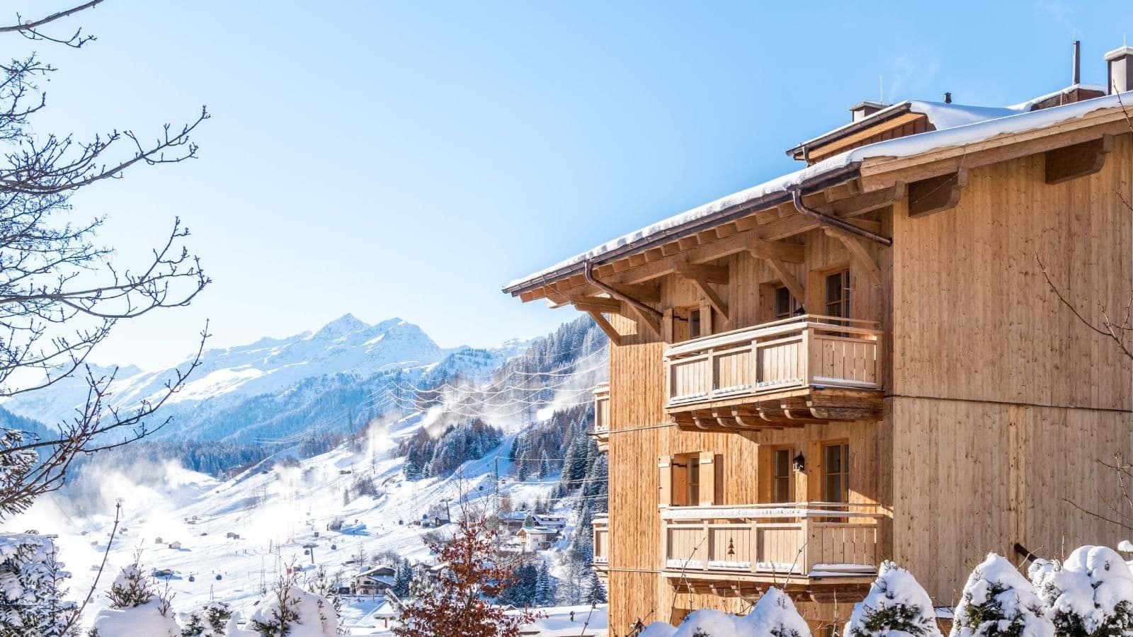 Timber chalet exterior with private balconies overlooking active ski slopes