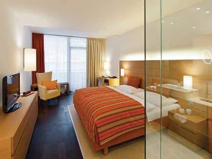 Bedroom with queen bed, flat-screen TV, and glass wall to ensuite