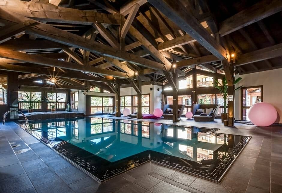 Indoor heated pool with exposed timber beams and poolside lounge seating