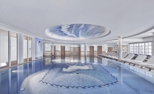 Indoor pool with horse mosaic tile and poolside lounge seating