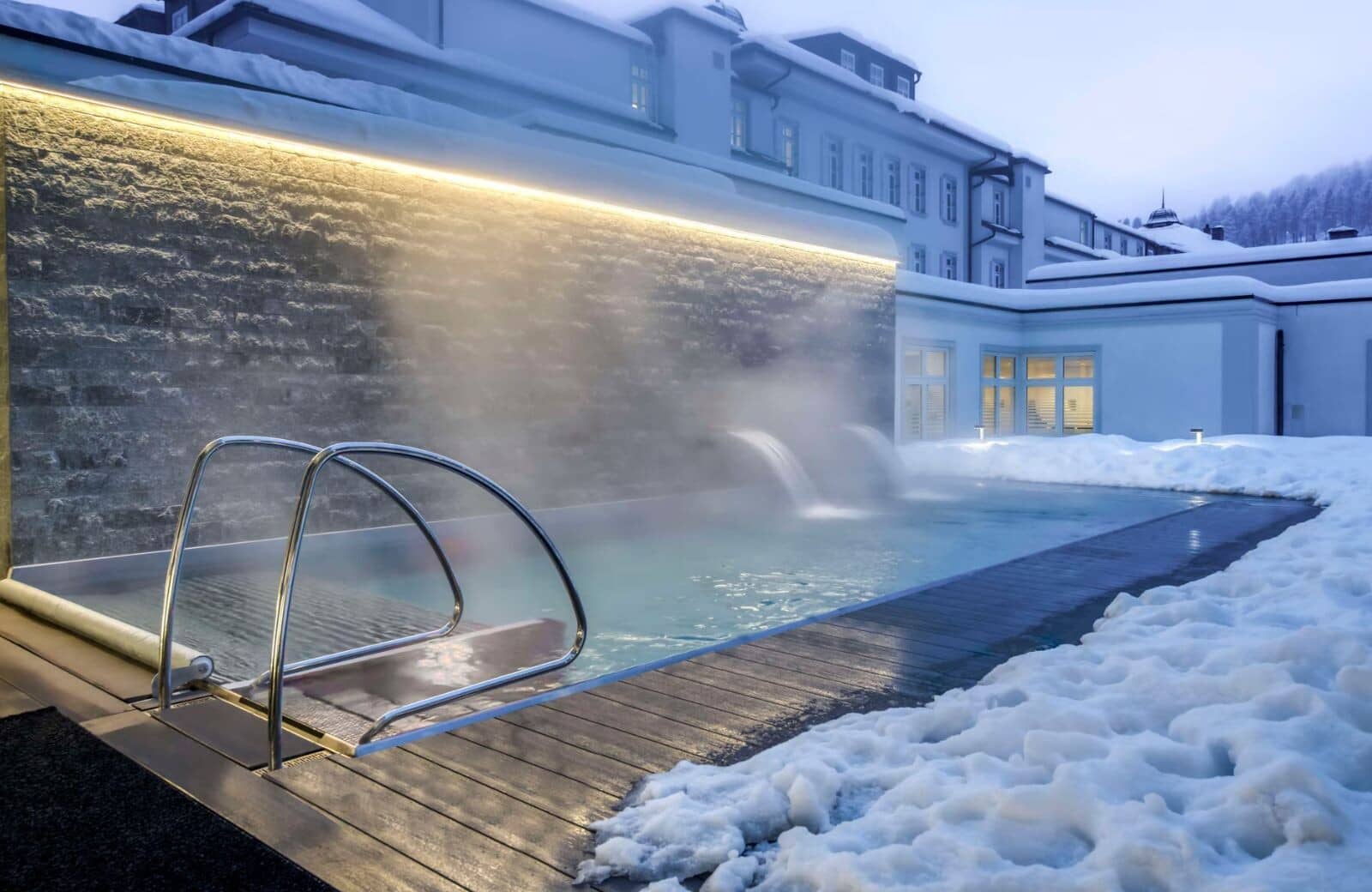 Heated outdoor pool with waterfall features and stone wall lighting