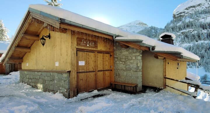 Chalet entrance with outdoor bench for gear; snowy mountain backdrop