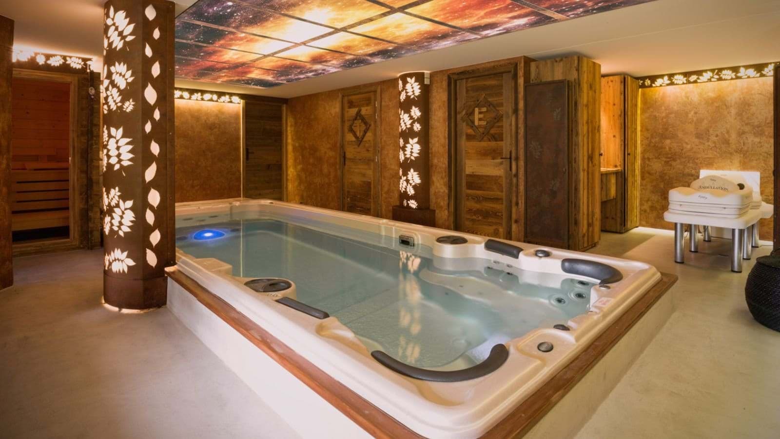 Indoor swim spa with adjacent wooden sauna and backlit ceiling
