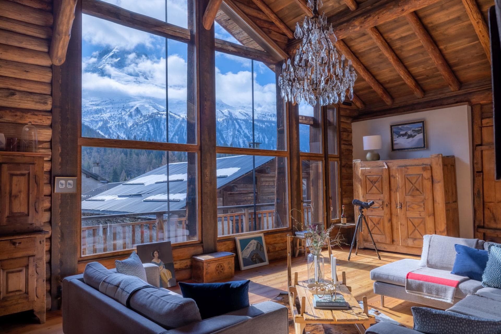 Log-walled living area with floor-to-ceiling mountain views and crystal chandelier