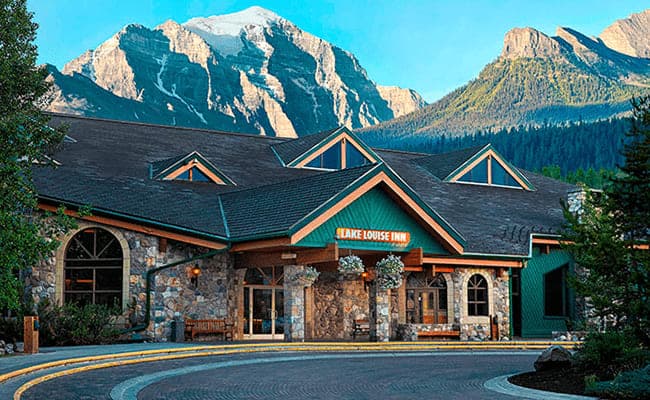 Stone lodge exterior with circular driveway and mountain backdrop