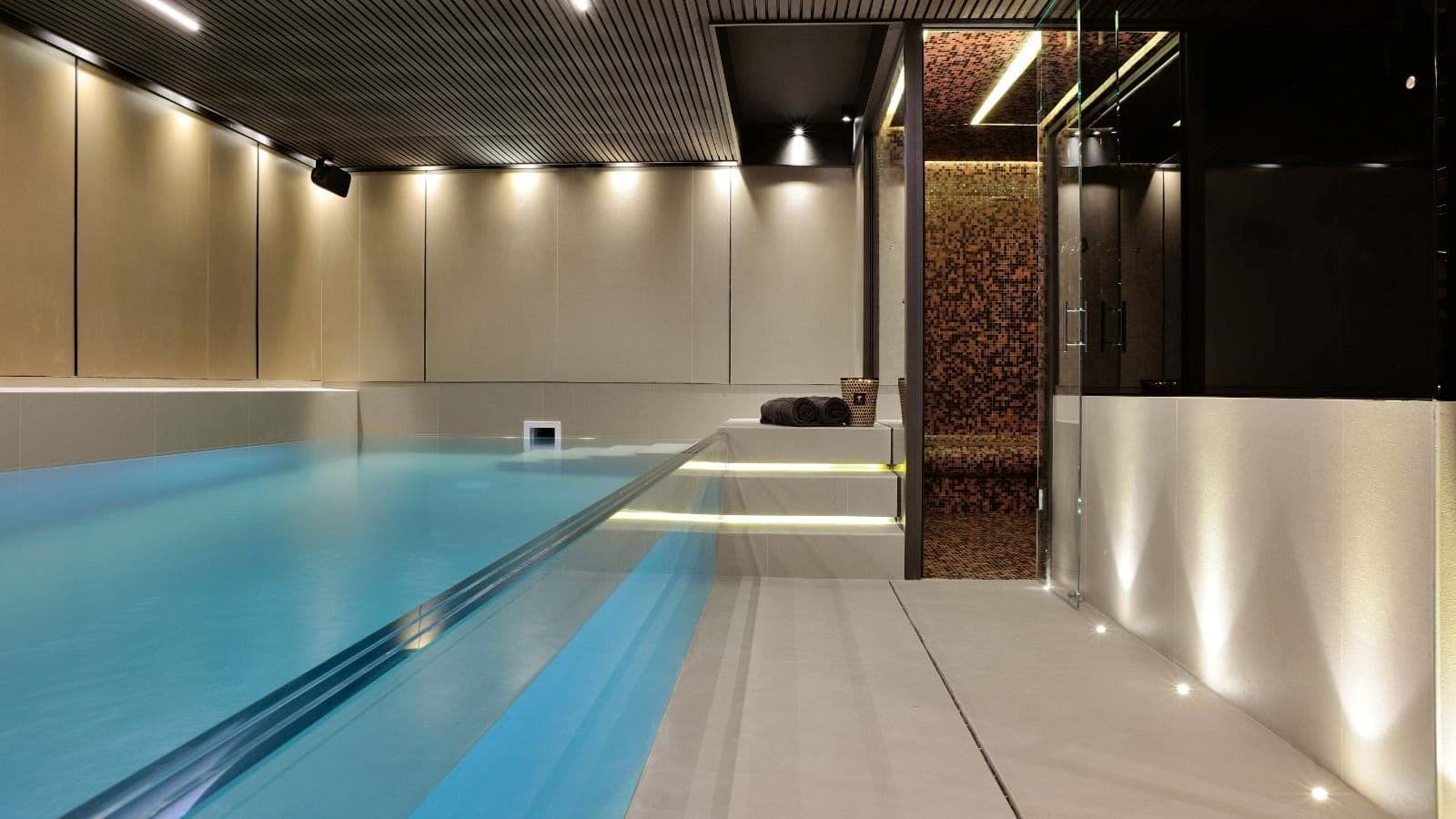 Indoor pool area with glass wall and adjacent mosaic-tiled steam room