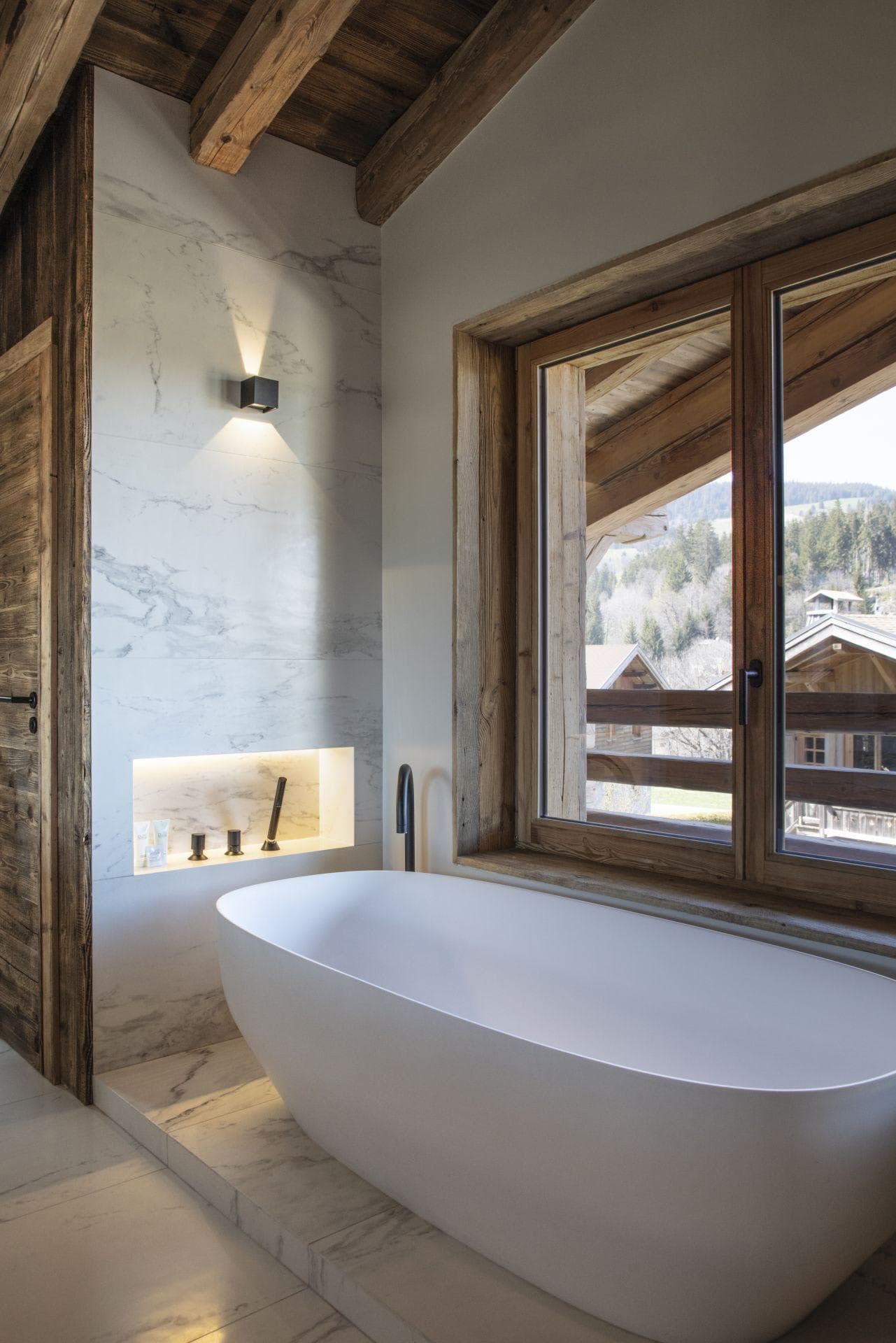 Freestanding soaking tub with mountain views and marble-clad wall