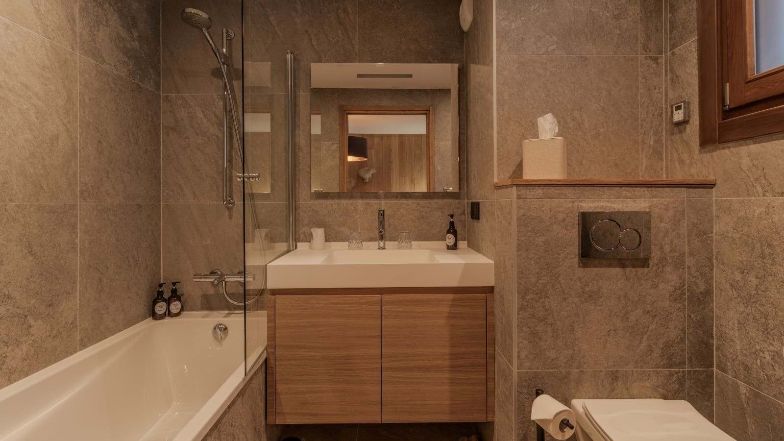 Bathroom with soaking tub, overhead shower, and stone tile walls