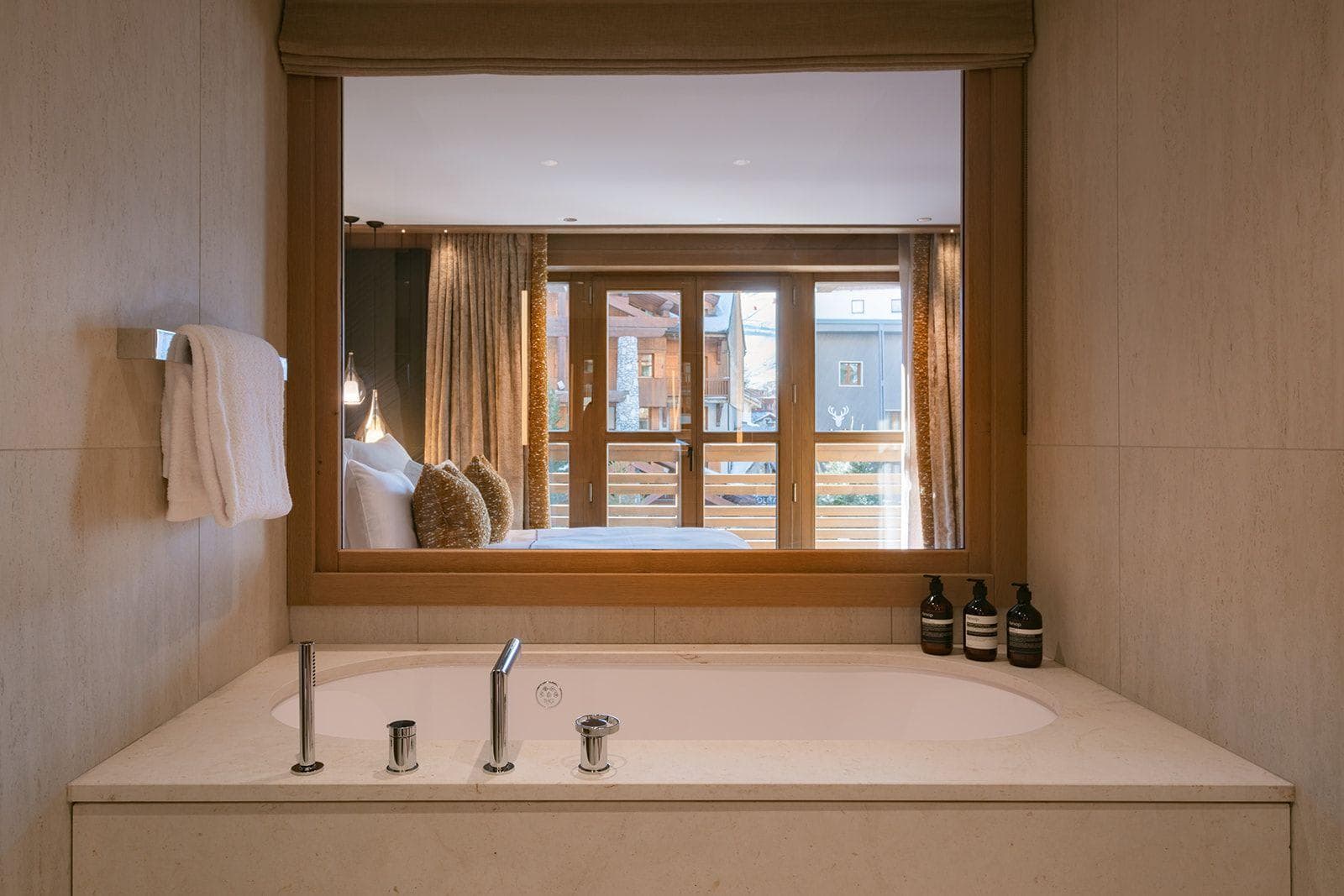 Soaking tub with internal window looking through bedroom to mountain balcony