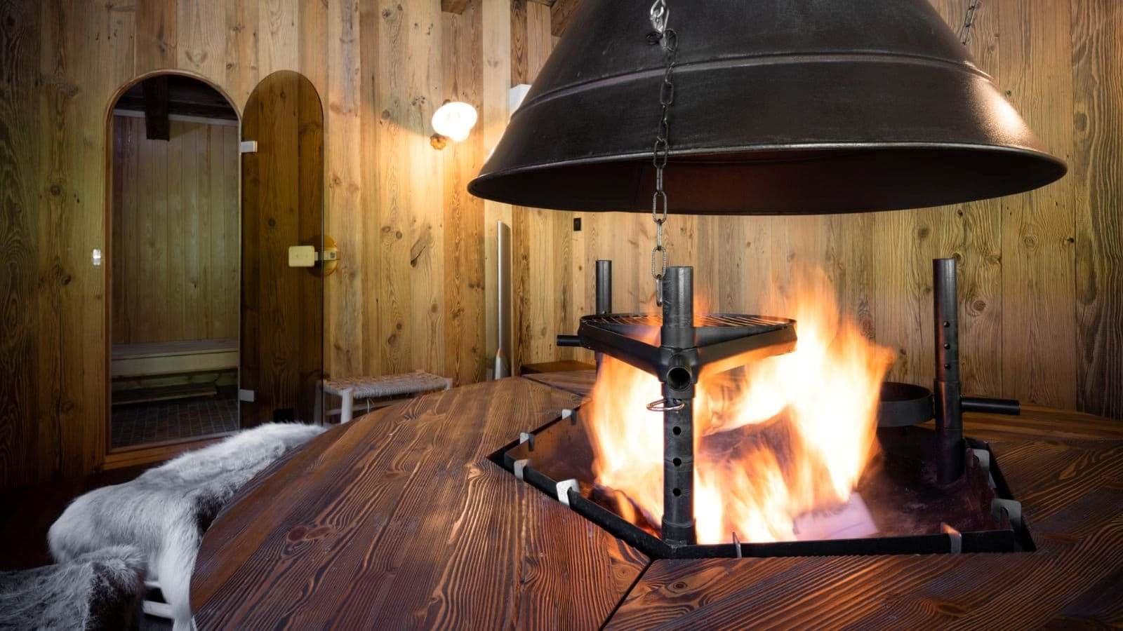 Indoor grill room with central fire pit and adjacent sauna access