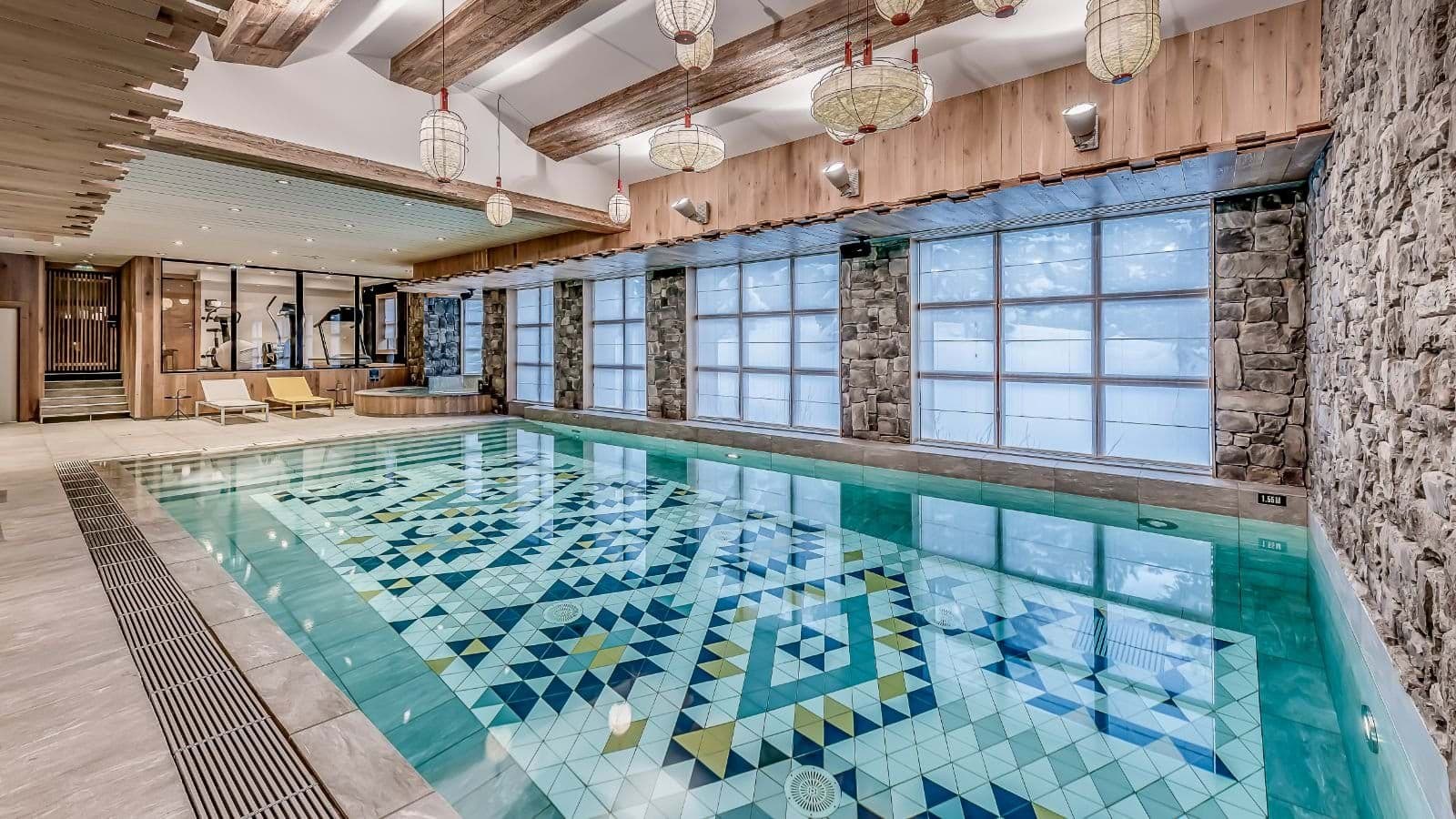 Indoor pool with mosaic tiling, adjacent hot tub, and glass-walled fitness center